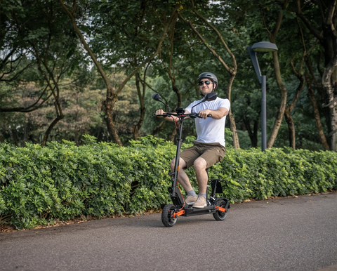 Male rider wearing helmet seated on JOYOR foldable electric scooter along tree-lined park pathway, comfortable seated summer commuting scene