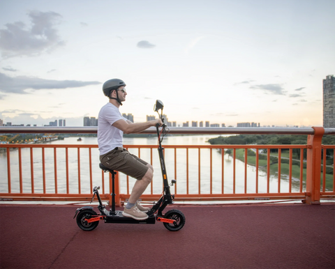Man riding seated JOYOR foldable electric scooter on riverside bridge during summer sunset, comfortable evening summer commute scene